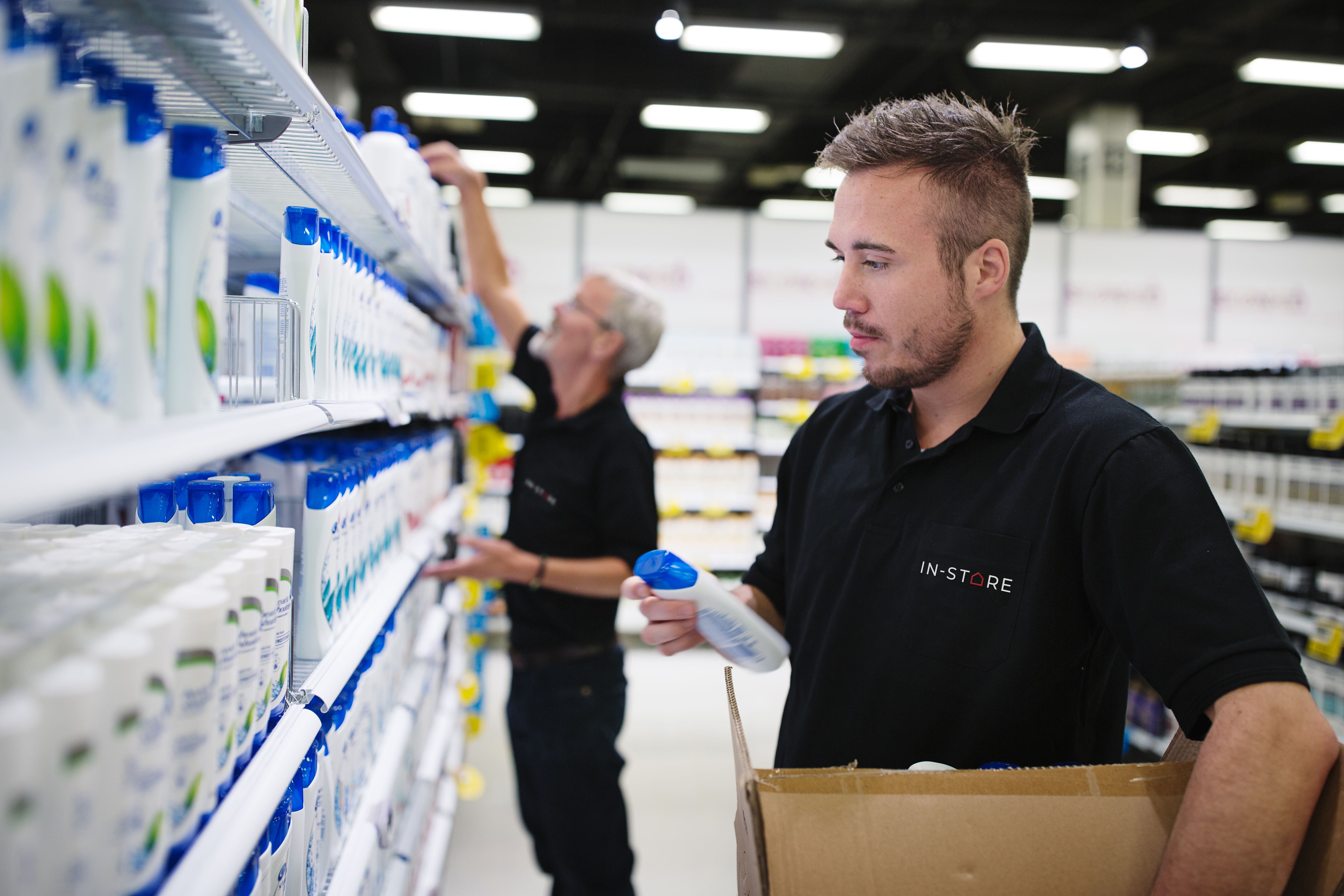 To mænd fylder produkter på hylder i et supermarked